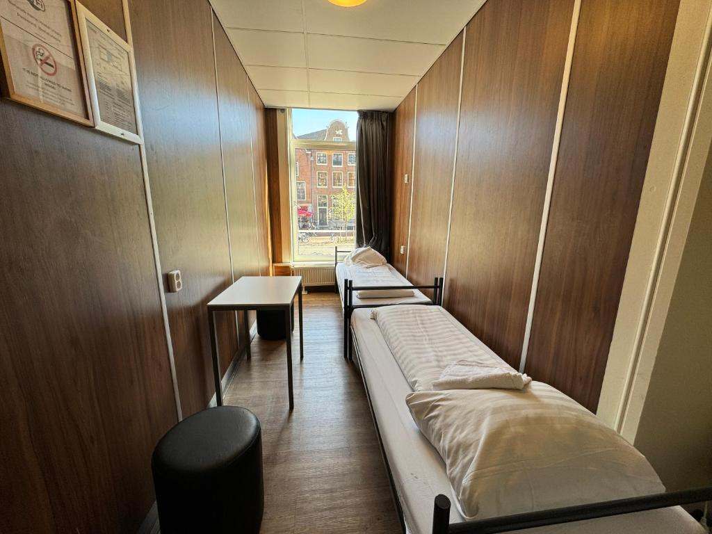 Long, narrow room with two single beds, a small table and a window at the end