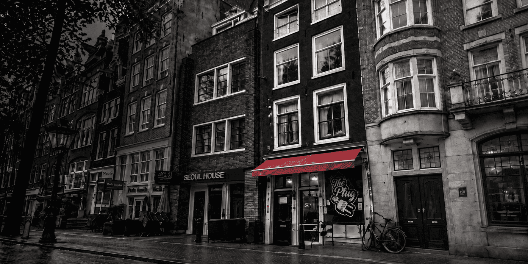 Black and white view of a canal street in Amsterdam with the red awning of Hostel Utopia