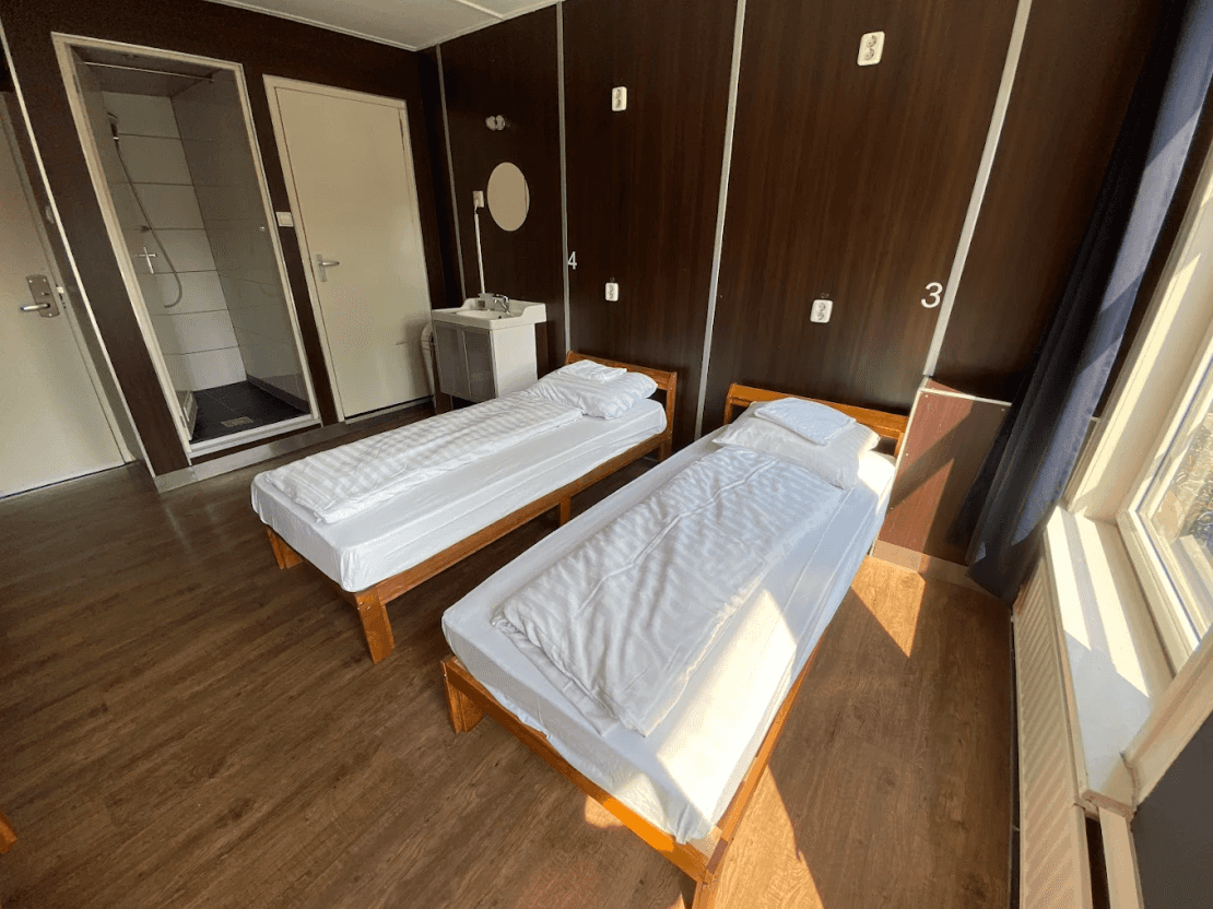 Room with two single beds, a small washbasin and a tiled shower cubicle by the door