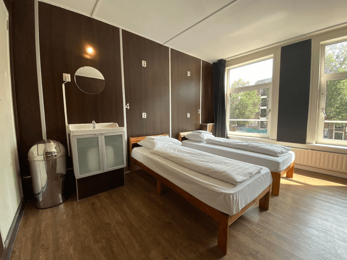 Bright room with two single beds, a washbasin and large windows looking out over the street