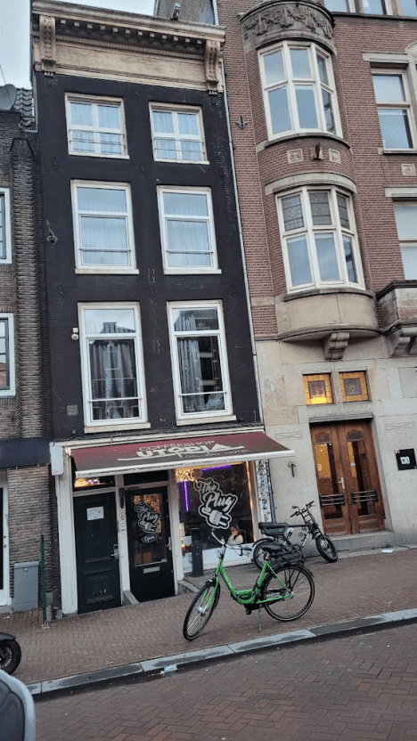 Tall, narrow brick canal house with the hostel entrance at street level and a bike parked outside