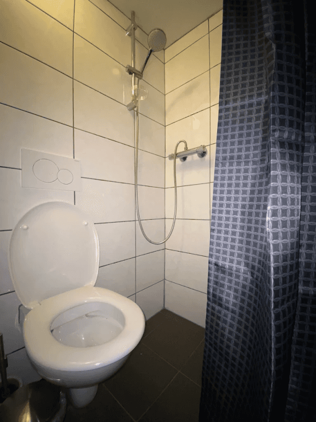 Small tiled bathroom with a toilet and a shower behind a curtain