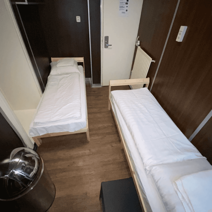 Two single beds with white linen on either side of a narrow room
