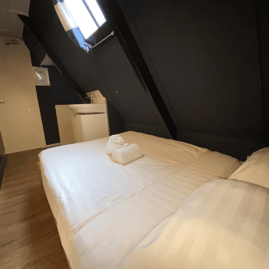 Double bed with rolled towels under a sloping ceiling with a skylight